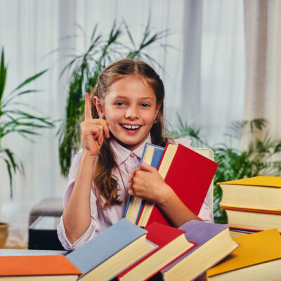 Cute little girl at the table with a lot of colorful books.