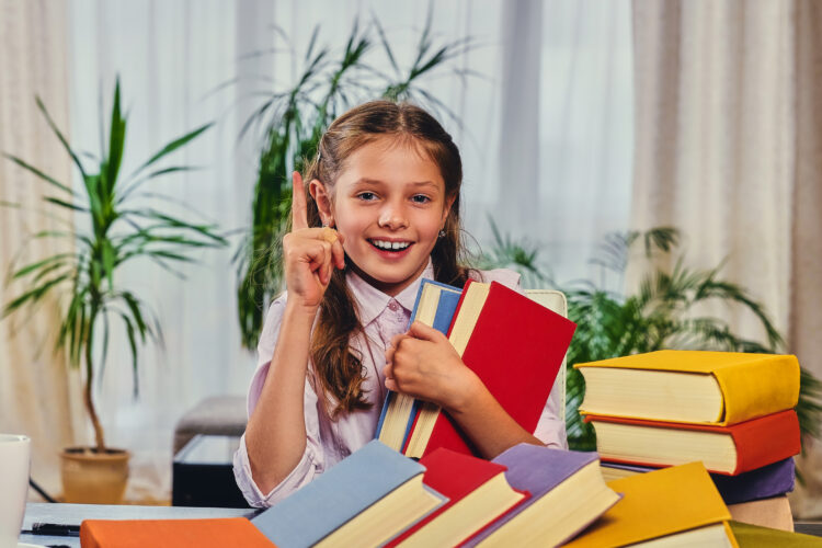 Cute little girl at the table with a lot of colorful books.